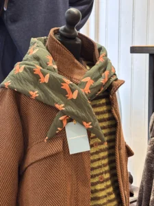 Paspop met een cognackleurige jas en een groene sjaal met oranje vogels